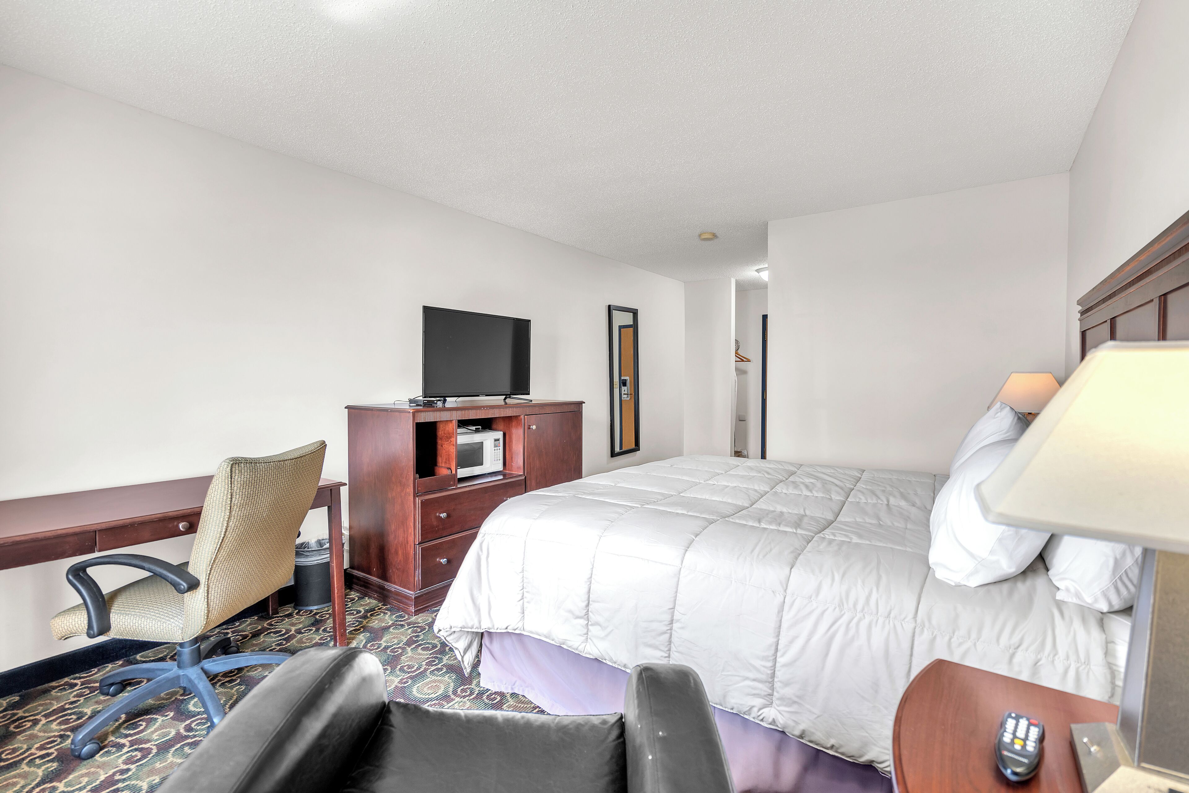 Una habitación de hotel con cama, escritorio, silla, televisor y lámpara.
