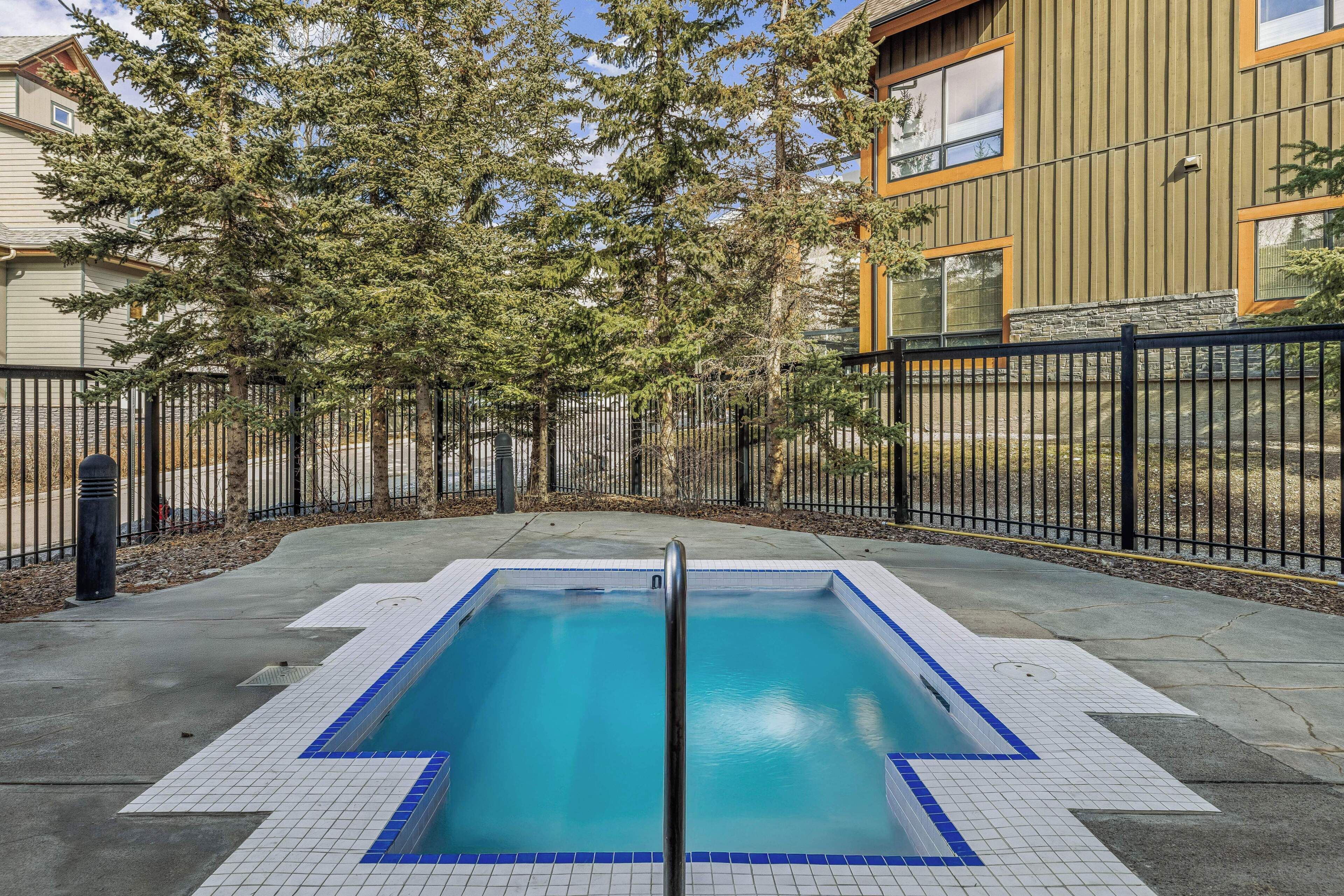 A rectangular pool with a blue border, surrounded by a black fence, and trees in the background.