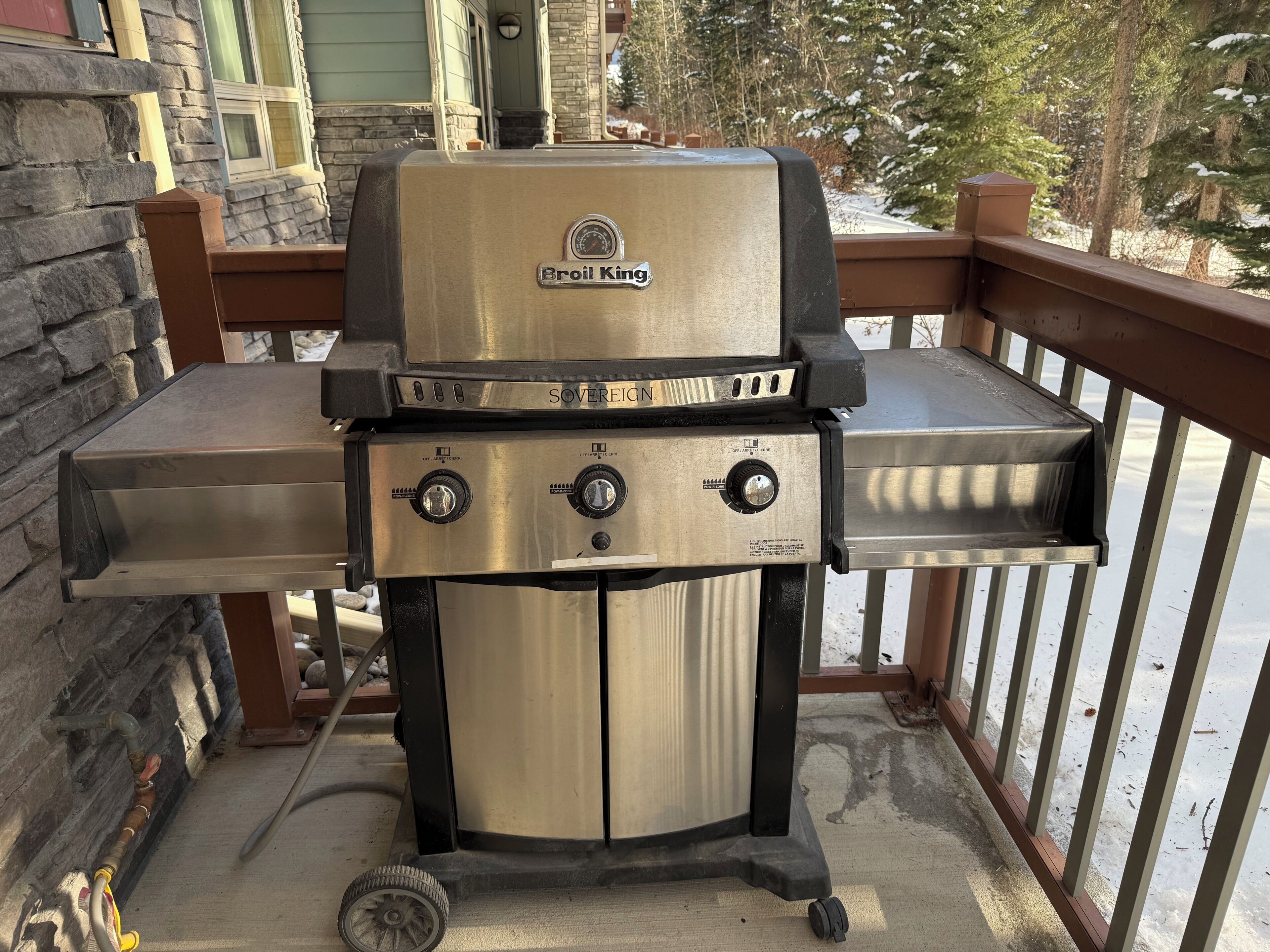 A Broil King grill with three control knobs, a digital display, and a gas supply line.