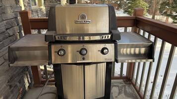 A Broil King grill with three control knobs, a digital display, and a gas supply line.
