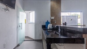 A modern kitchen with a black countertop, a large blue water dispenser, and a window with a view. - Apartamento Para 6 com Vaga e Churrasqueira (Para de Minas)