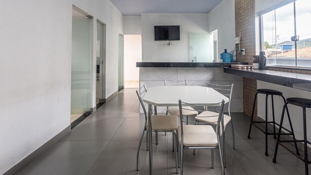 A modern kitchen with a dining area, a TV mounted on the wall, and a large window. - Apartamento Para 6 com Vaga e Churrasqueira (Para de Minas)