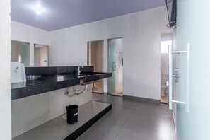A modern bathroom with a black countertop, a sink, a mirror, and a glass shower door. - Apartamento Para 6 com Vaga e Churrasqueira (Para de Minas)