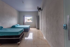A room with two beds, a ceiling fan, a window with curtains, and a refrigerator. - Apartamento Para 6 com Vaga e Churrasqueira (Para de Minas)