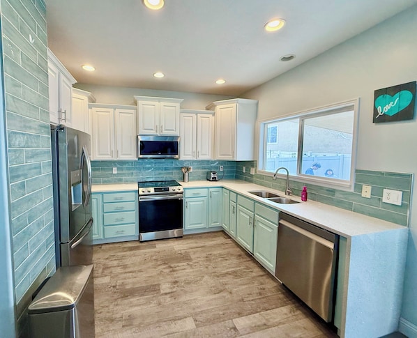 A kitchen with light blue cabinets, a stainless steel refrigerator, a microwave, an oven, a dishwasher, and a window with a view. - Spacious 4-bedroom house in beautiful West Jordan with AC and gym (West Jordan)