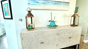 Un salon moderne agrémenté d’une console au motif décoratif, de deux lanternes fixées au mur, d’une œuvre d’art encadrée et d’une plante ornementale.