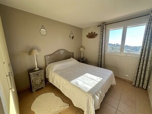 Ein Schlafzimmer mit einem Bett, zwei Nachttischen, einem Fenster mit Vorhängen, einer Wanddekoration und einer Tür.