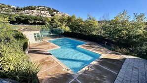 Una piscina rectangular con solárium empinado, rodeada de vegetación y una colina al fondo.