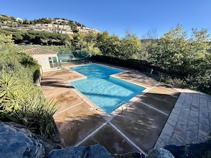 Ein rechteckiger Pool mit gefliestem Sonnendeck, umgeben von Grünflächen und einer Hügelkulisse.