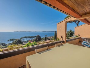A terrace with a table and chairs, overlooking a coastal view with trees and a clear sky. - APARTMENT WITH PANORAMIC SEA VIEW (STE MAXIME)
