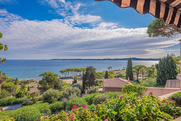 A coastal landscape with a view of the sea, a garden with pink flowers, and a building with a tiled roof. - APARTMENT WITH PANORAMIC SEA VIEW (STE MAXIME)