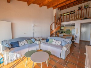 A living room with a sofa, two small tables, a staircase, and a kitchen in the background. - APARTMENT WITH PANORAMIC SEA VIEW (STE MAXIME)