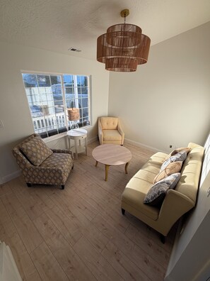 Un salón con un sillón estampado, un sofá con almohadones, una mesita redonda y una lámpara colgante.