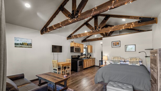 Een knus ingerichte kamer met een bed, een klein tafeltje, een zithoek en een kitchenette, afgewerkt met houten balken.