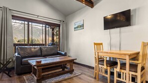 Een woonkamer met een bank, salontafel, houten eettafel, stoelen en een aan de muur bevestigde televisie.