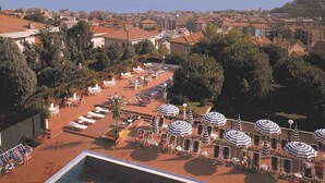 Area piscina con lettini e ombrelloni, circondata da edifici e alberi.