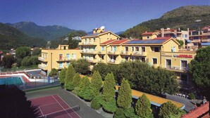 Un hotel a più piani con balconi, una piscina e montagne sullo sfondo.