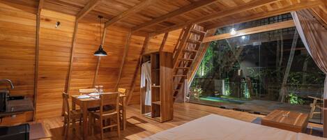 Una baita di legno con camera da letto soppalcata, zona pranzo e vista sull'esterno.