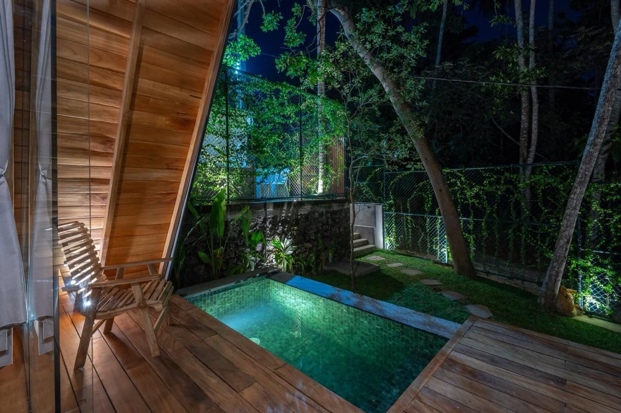 A wooden deck with a small pool, surrounded by a stone wall and greenery.