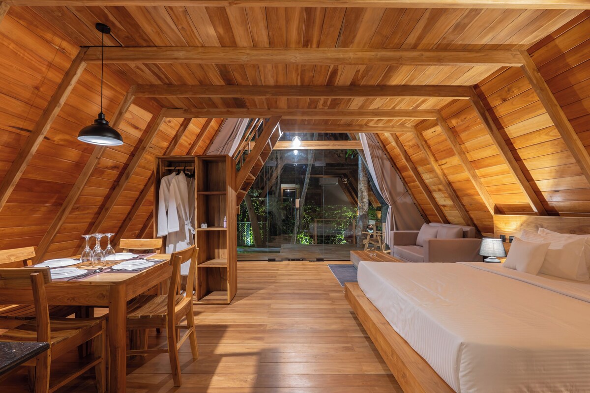 Una habitación estilo ático con techo de madera, una cama, un escritorio con sillas y una mesa de comedor.