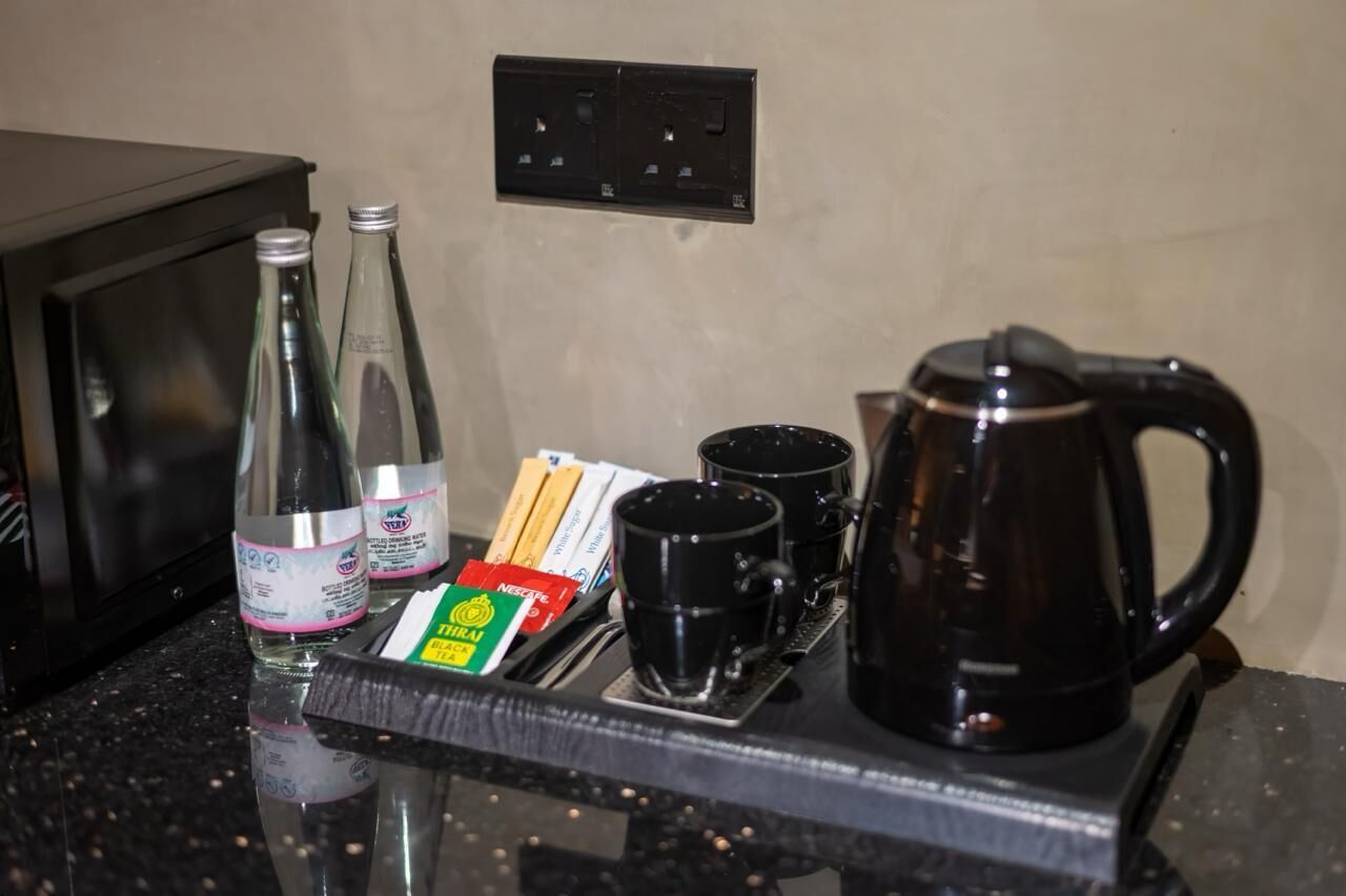 A kitchen counter with a coffee maker, two bottles, a tray with cups and a box of tea bags.