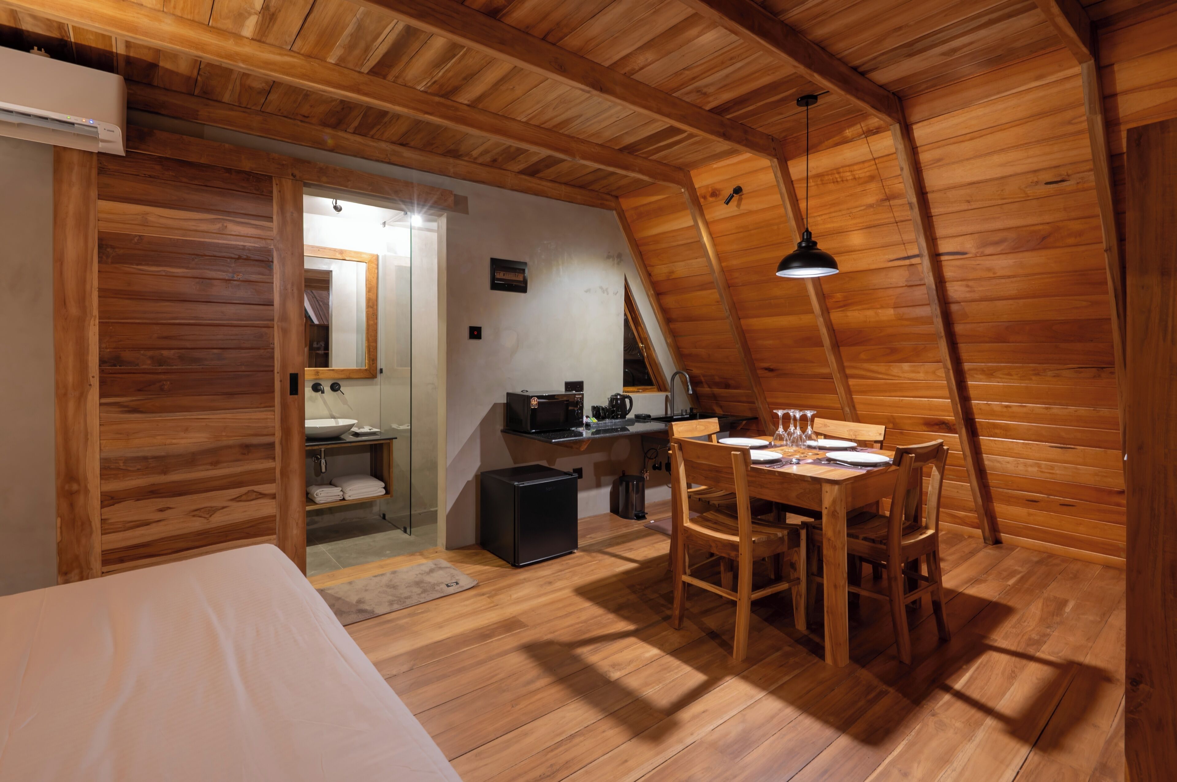 A wooden interior with a dining table, chairs, a small kitchen area, and a bed.