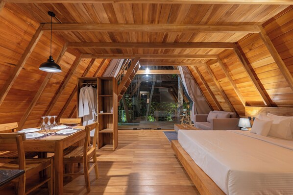 An attic-style room with a wooden ceiling, a bed, a desk with chairs, and a dining table.