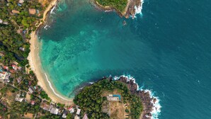 An aerial view of a coastal area with a beach, a small building, and surrounding vegetation. - Ceylon Canopy (Dickwella)