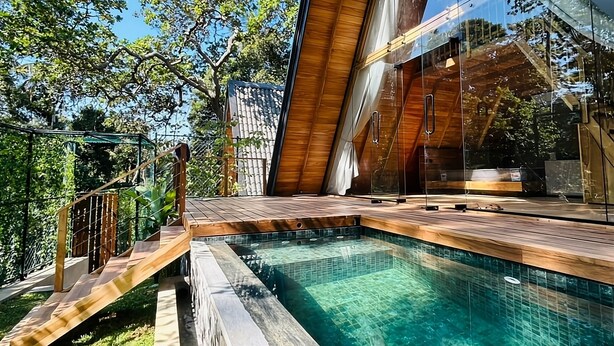 A modern outdoor pool area with a wooden deck and glass walls. - Ceylon Canopy (Dickwella)
