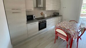 Une cuisine moderne équipée d’un four à micro-ondes, d’un grille-pain et d’un four traditionnel, une table à manger avec des chaises, et une vue sur l’extérieur.