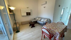 Un espace de vie compact comprenant un canapé, une table à manger avec des chaises, une lampe sur pied et un système de climatisation intégré.