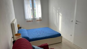 Une chambre à coucher avec un lit, une table de chevet, une lampe, une fenêtre avec des rideaux et une porte.
