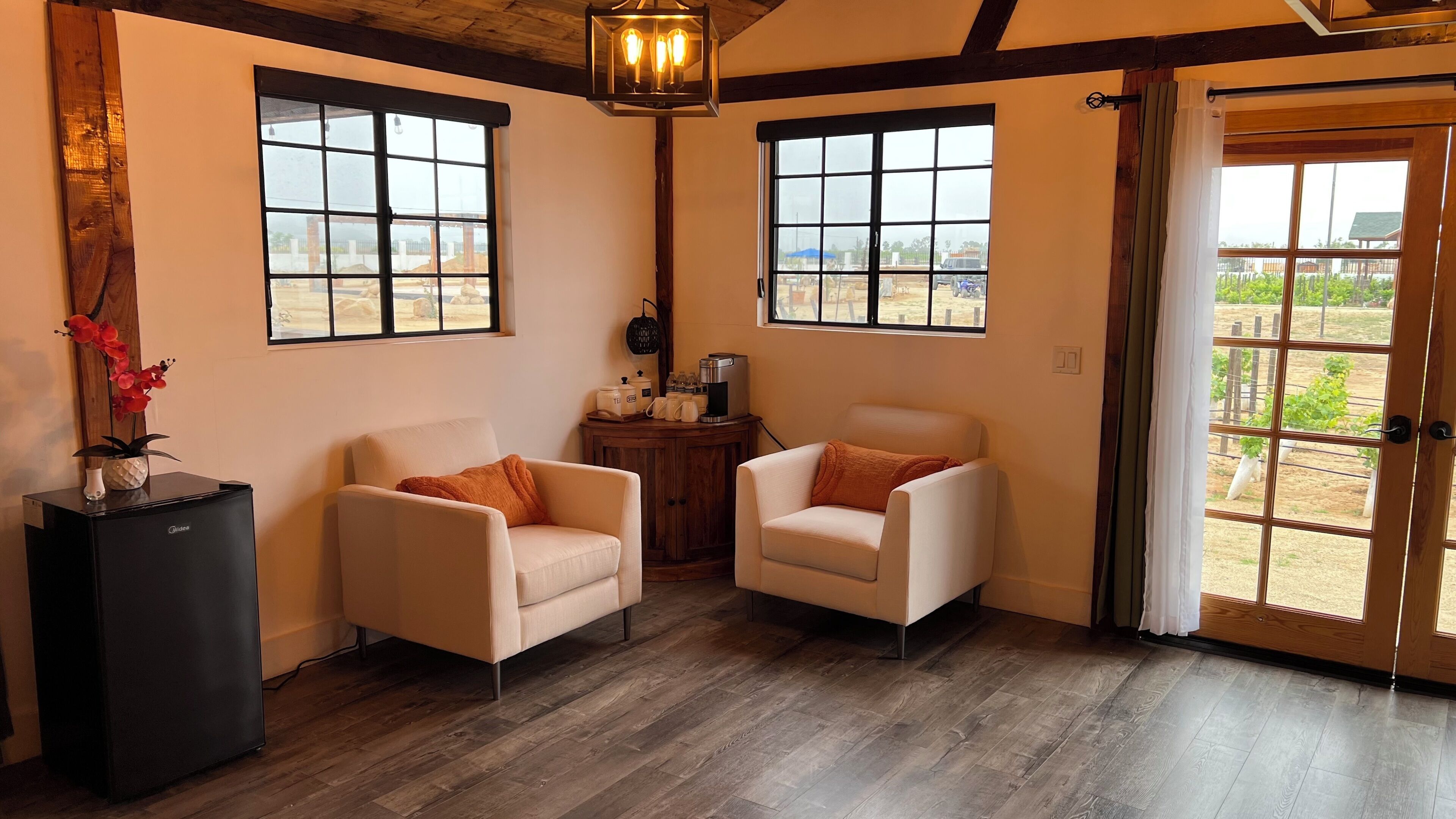 Una habitación con dos sillones blancos, un mueble bajo con cafetera y una puerta que da a un espacio exterior.