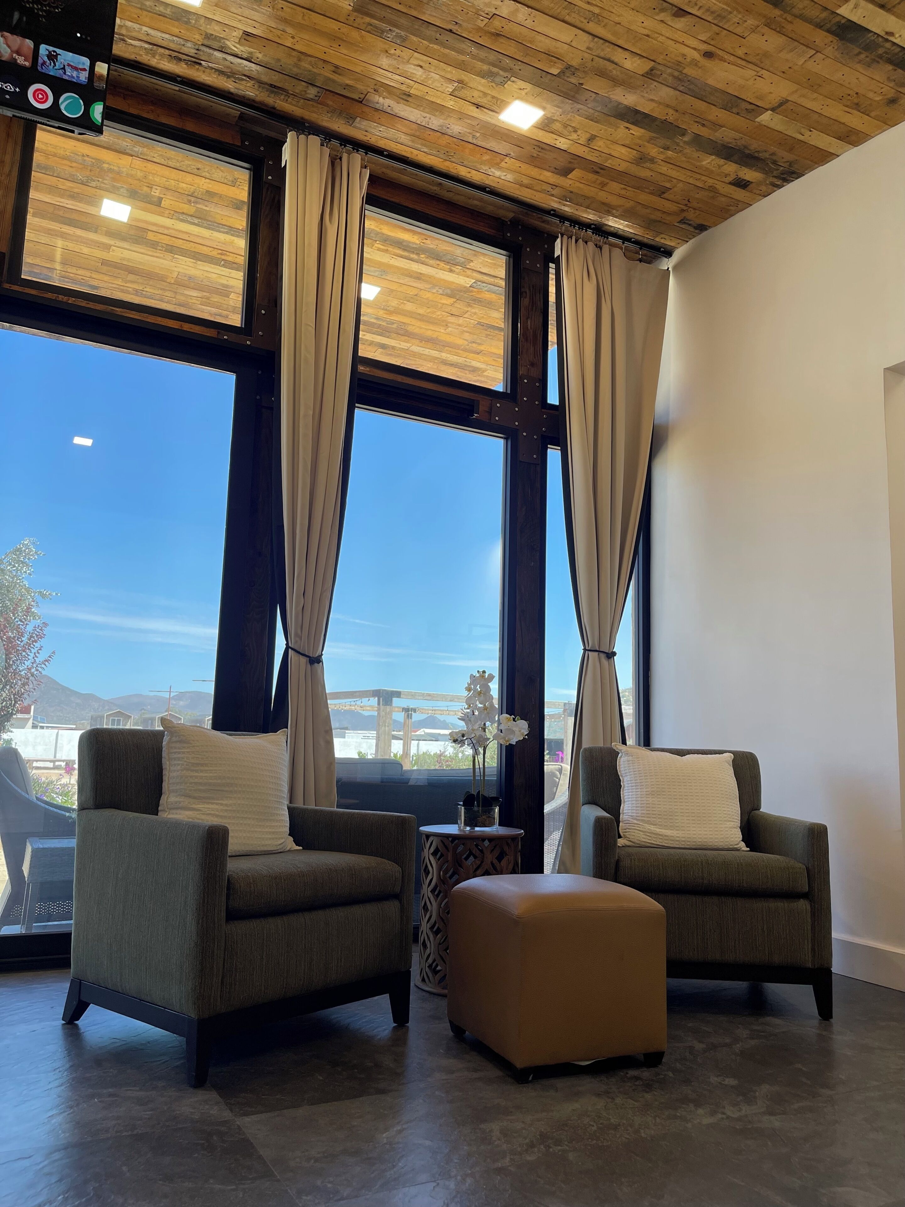 A room with two armchairs, a small ottoman, and large windows with curtains.