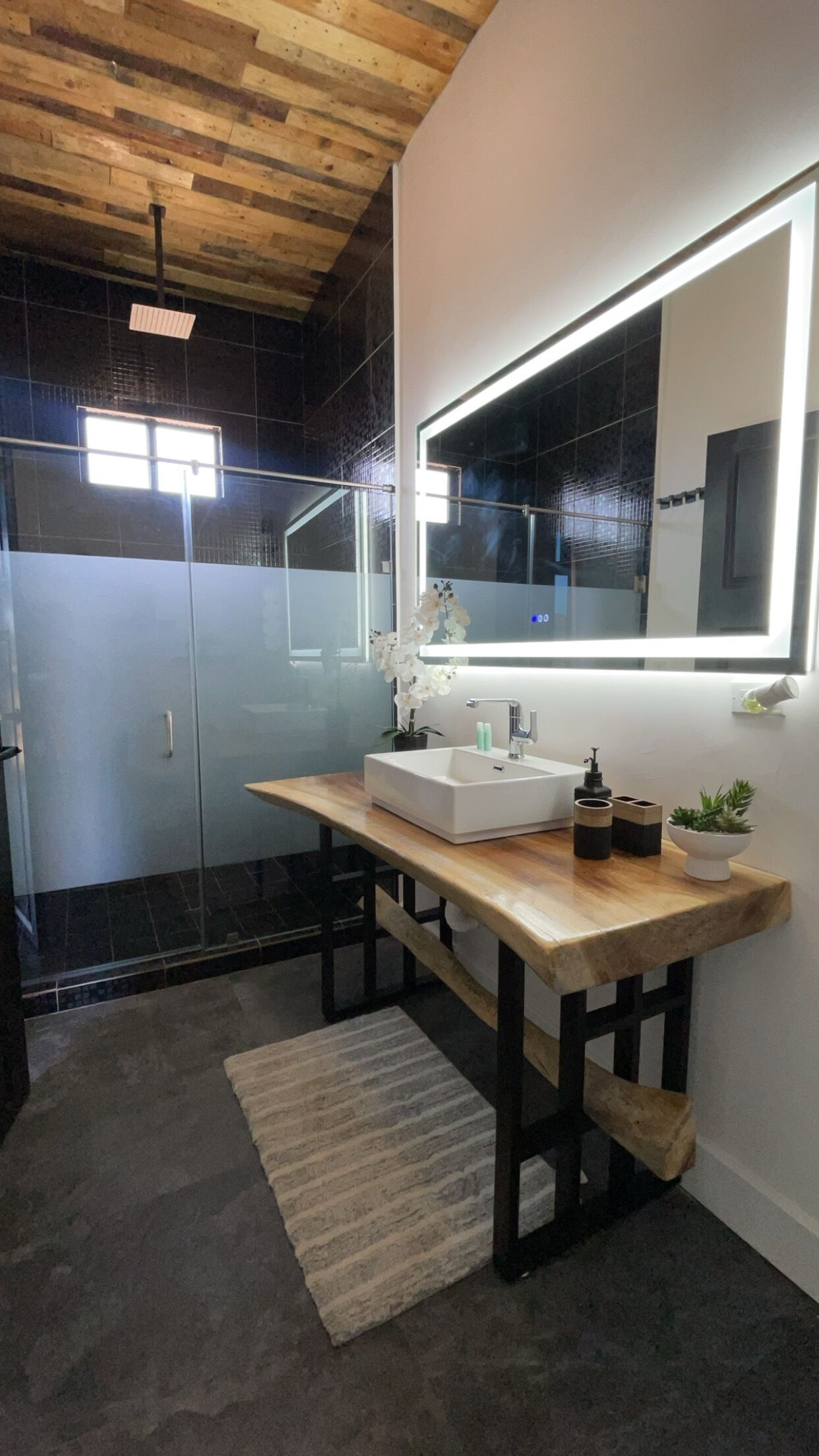 A modern bathroom with a wooden vanity, a large mirror, and a glass shower enclosure.