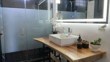 A modern bathroom with a wooden vanity, a large mirror, and a glass shower enclosure.