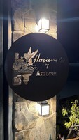 Uma placa com design de pássaro e folhagem, o texto 'Hacienda 7 Amores' e duas luzes de parede.