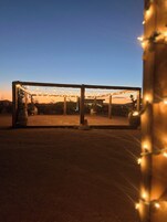Un espacio al aire libre cubierto con luces colgantes, vigas de madera y cielo despejado.