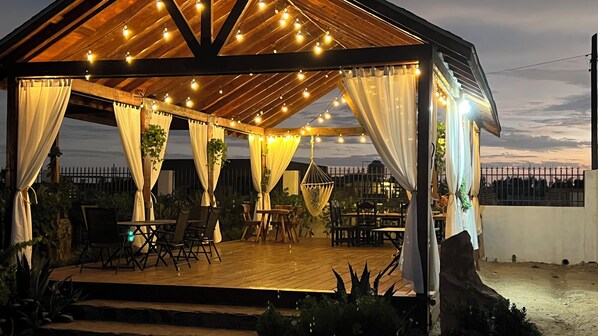 A covered outdoor patio with string lights, wooden furniture, and curtains. - Hacienda 7 Amores (Valle de Guadalupe)