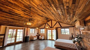 Amplia habitación con vigas de madera en el techo, ventanas grandes y una cama.