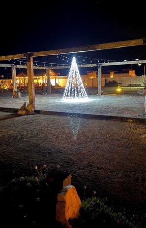 A nighttime outdoor area with a lit fountain, wooden structures, and a paved surface. - Hacienda 7 Amores (Valle de Guadalupe)