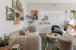 A living room with a sofa, armchair, coffee table, and artwork on the walls. - Ashry Collective-Ocean & Mountain Views (Cape Town)