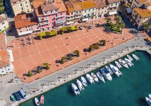 An aerial view of a coastal area with a tiled square, boats docked along the shore, and buildings with balconies. - Casa Marlù - Spacious apartment in the historic centre of Porto Azzurro (Porto Azzurro)