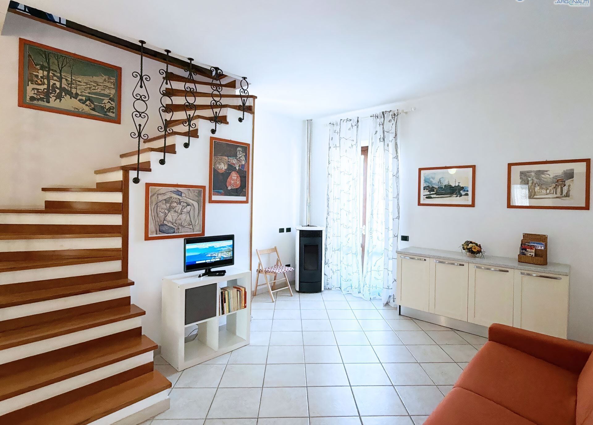 Una sala de estar con una escalera de madera, un televisor, una chimenea y un comedor con un armario y una silla.