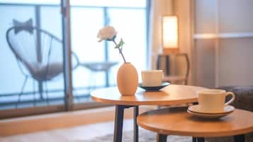 Una habitación acogedora con una mesa redonda de madera, un florero con una sola flor, dos tazas blancas y una silla con diseño de pajarita.