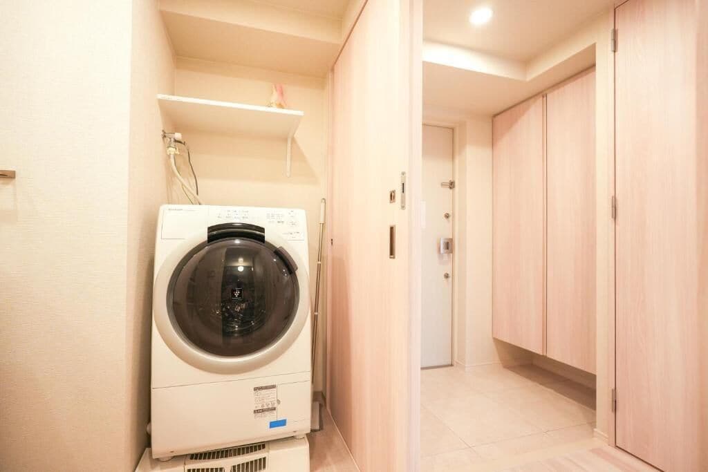 A laundry area with a washing machine, a shelf above it, and a wooden wardrobe in a hallway.