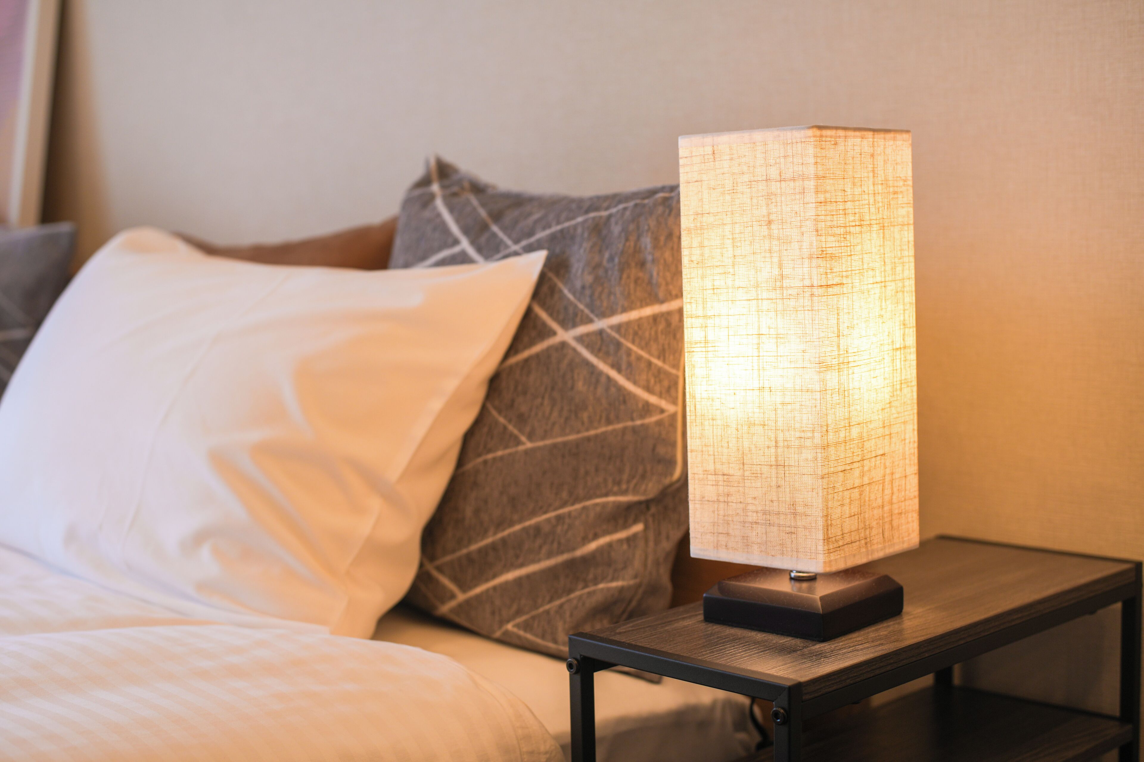 A bed with white bedding, a gray pillow with a leaf pattern, and a bedside table with a lamp.