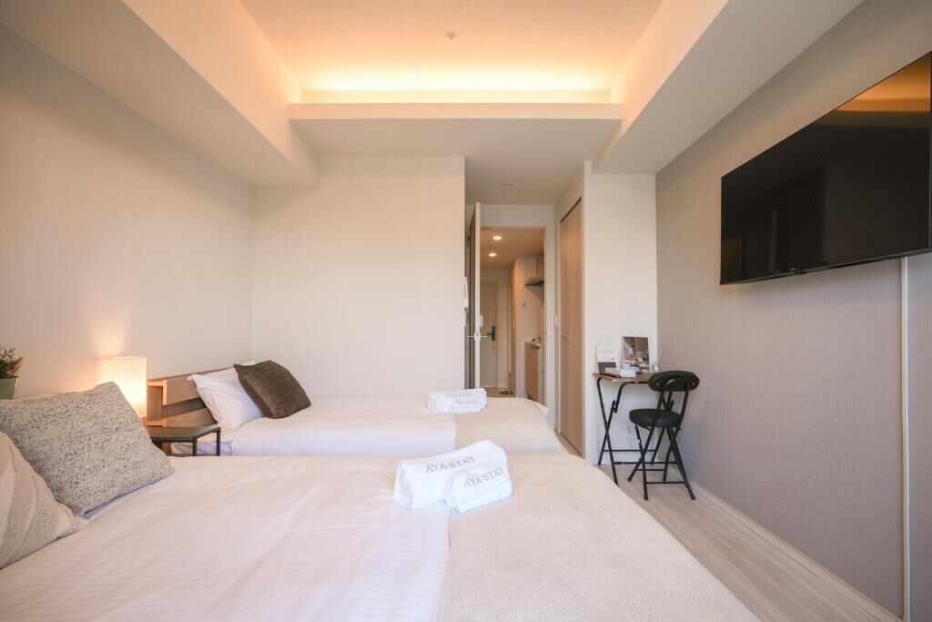 Une chambre d’hôtel avec deux lits, un bureau, une chaise et un téléviseur fixé au mur.