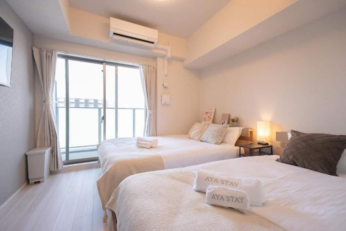 Une chambre d’hôtel avec deux lits, une fenêtre avec des rideaux, une table de chevet avec une lampe et un appareil de climatisation.