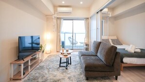 A modern living room with a flat-screen TV, a sofa, a coffee table, and a large window with a view. - AYA RESIDENCE (Osaka)